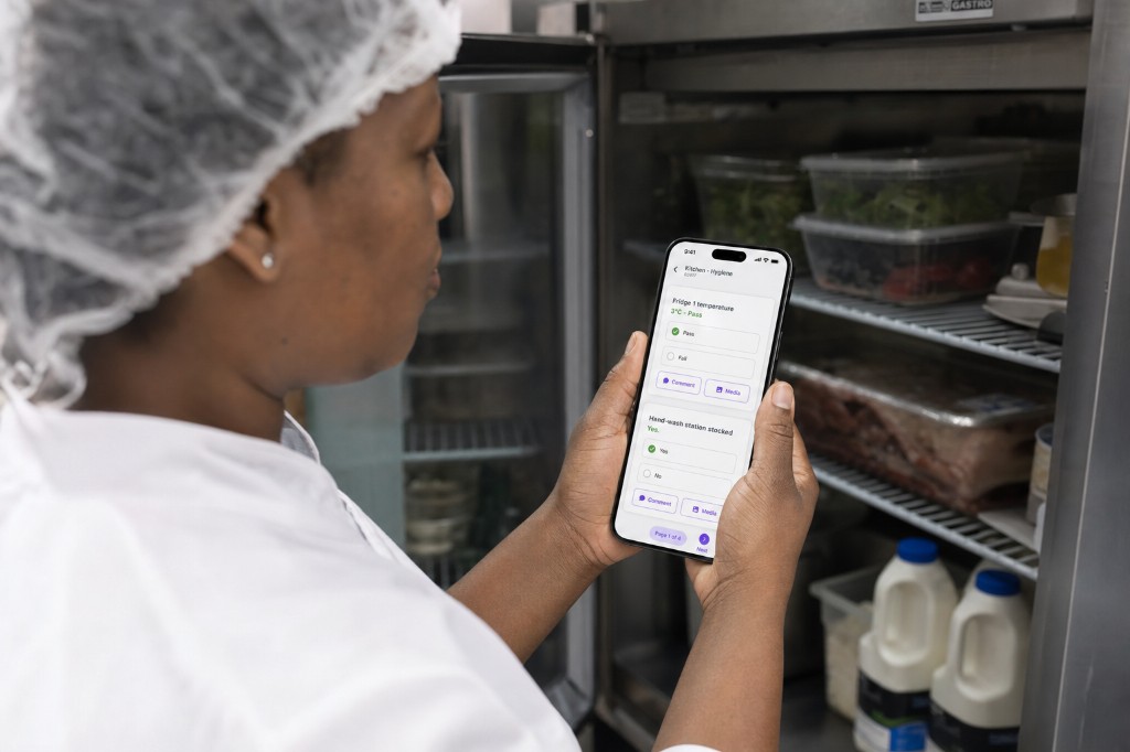 Kitchen staff member recording a passed fridge temperature on a phone during a hygiene check